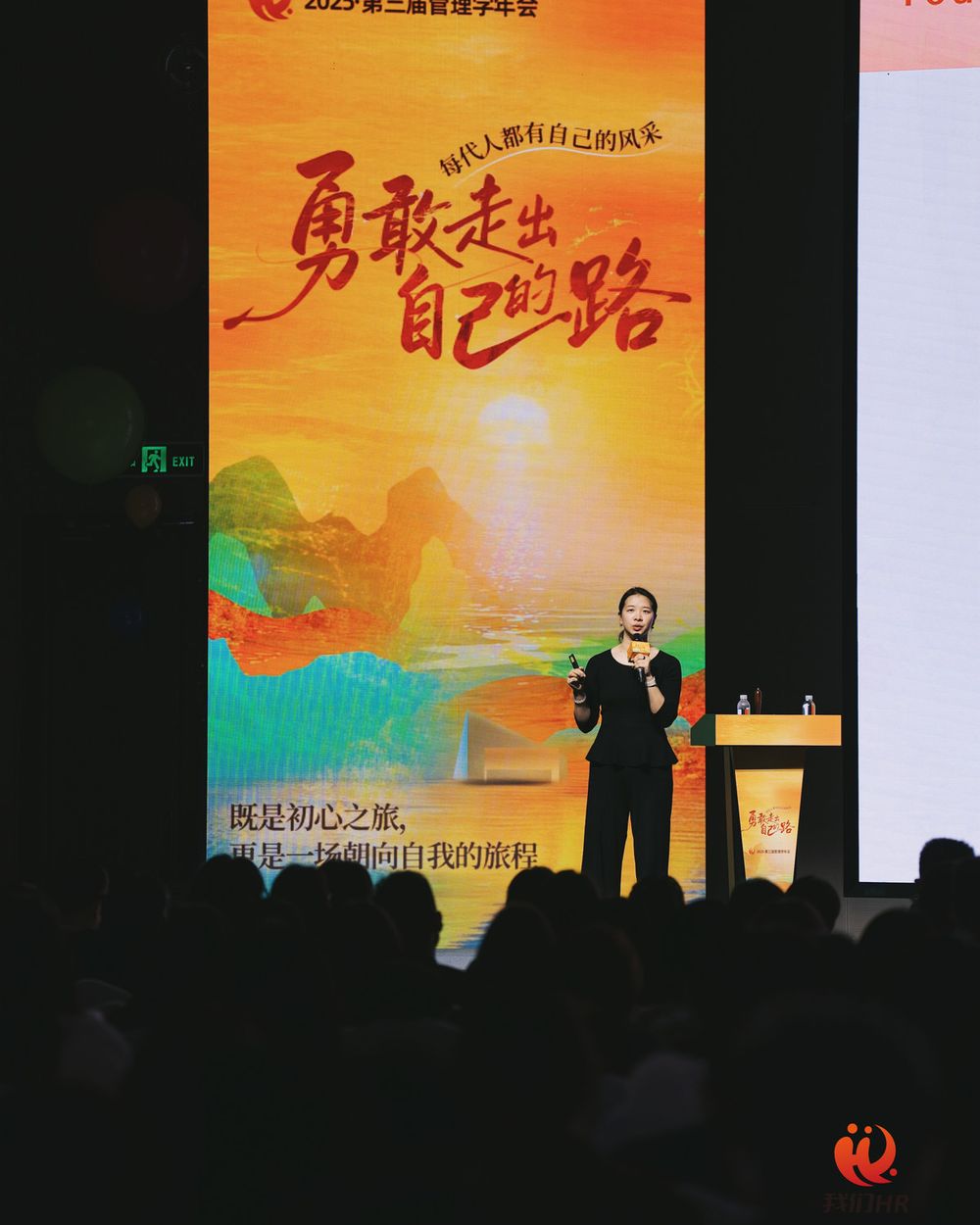 Marcia delivering a keynote on a large stage under a painted poster